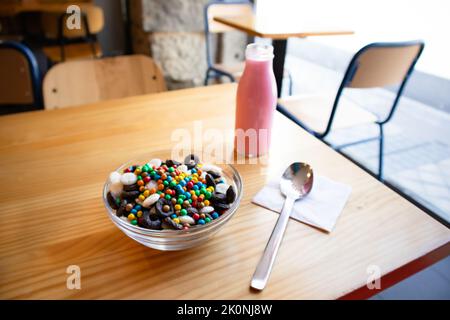 Colazione a secco in ciotola di vetro su un tavolo di legno nel caffè. Deliziosi cornflakes e latte rosa in una bottiglia. Colazione sana e utile. Cibo per Foto Stock