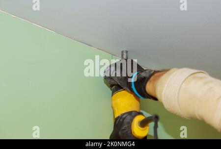 Utilizzando un cacciavite e delle viti per cartongesso, un operatore avvita il cartongesso in posizione sul soffitto Foto Stock