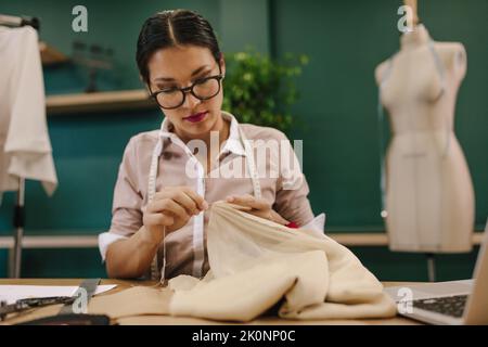 Abito con cuciture a mano di design femminile in studio di moda. Donna asiatica su misura che lavora nel suo laboratorio. Foto Stock