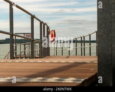 Nuovo molo con una salvagente rossa di fronte ad un lago. L'anello di sicurezza sulla ringhiera è un'attrezzatura per il salvataggio di una persona in acqua in una spiaggia balneabile. Foto Stock