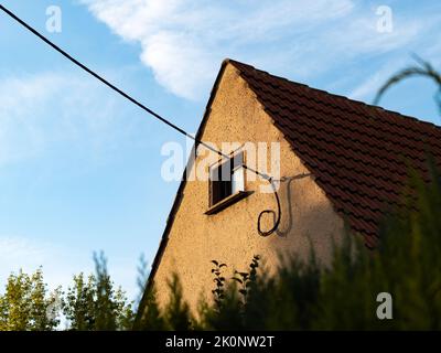 Edificio residenziale con un cavo sulla parete esterna. Tetto a capanna con tegole rosse e una piccola finestra sulla facciata. Vecchia architettura nella Germania orientale. Foto Stock