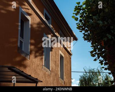 Facciata rinnovata di un vecchio edificio vicino ad un grande albero. Vista dall'angolo basso verso l'esterno. Le finestre e la grondaia sul tetto sono caratteristiche dell'edificio. Foto Stock