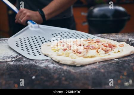 Pizza su una spatola prima di cuocere in forno. Il processo di preparazione della pizza fatta in casa. Il concetto di fast food fatto in casa. Vista frontale. Foto Stock