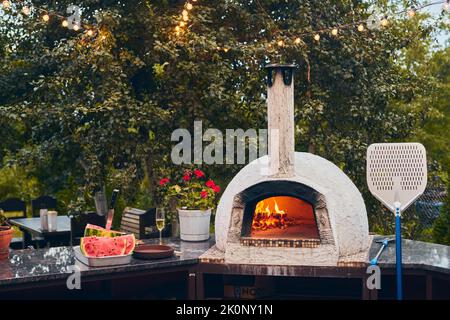 Forno a legna per pizza con tronchi di betulla per l'accensione. Il fuoco brucia e il forno si riscalda. Vista frontale. Foto Stock