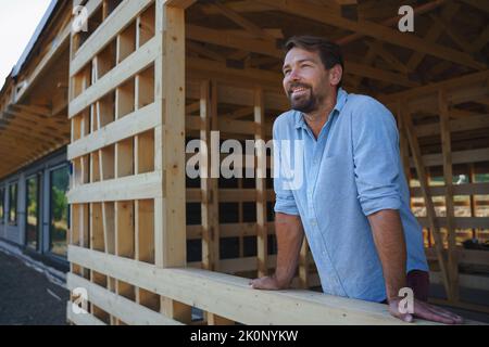 Uomo che guarda fuori dalla sua casa incompiuta, costruzione di eco-casa ecologica rinnovabile a basso consumo energetico sostenibile in legno . Foto Stock