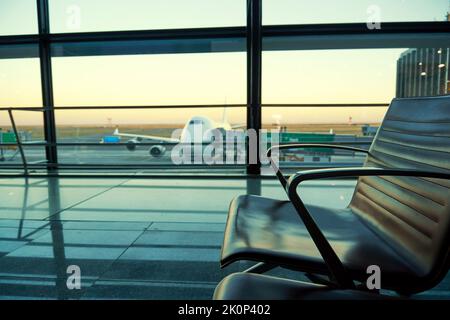 Sedie nella lobby dell'aeroporto e silhouette di aerei al crepuscolo. Viaggi e trasporti aerei sfondi Foto Stock