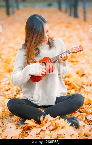 Ukulele in mani donna closeup suonare uno strumento acustico ukulele in autunno all'aperto Foto Stock
