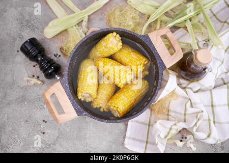 Pannocchie di mais cucinate in pentola su tabella grigia di cemento Foto Stock