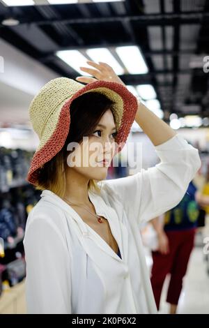 Donna asiatica prova un cappello in un negozio Foto Stock