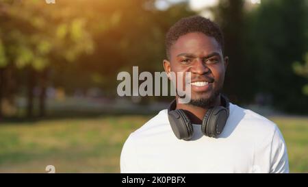 Sorridente afroamericano con cuffie cammina nel parco Foto Stock