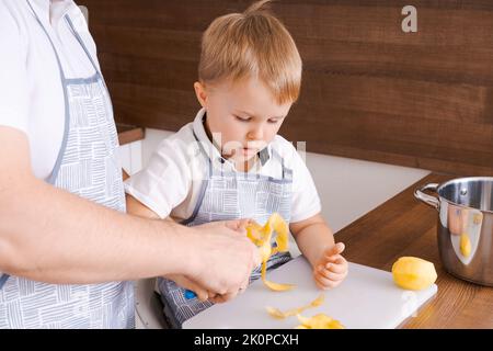 Concetto di cibo e nutrizione. Foto di due allegri papà e figlio che si posano in cucina peeling patate andando a cucinare cibo vegetariano per cena insieme, indossando grembiuli identici Foto Stock