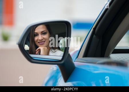 Donna soddisfatta guarda il proprio riflesso nello specchietto retrovisore Foto Stock