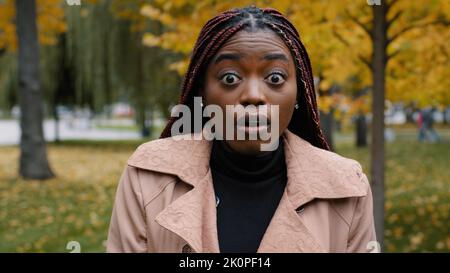 Primo piano stordito afro-americano donna in piedi all'aperto guardando la fotocamera con gli occhi spalancati e la bocca sensazione shock sorpresa da notizie inaspettate Foto Stock