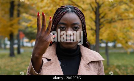 Primo piano seria focalizzata afro-americana donna in piedi all'aperto guardando la macchina fotografica contando da uno a cinque conteggi dita sulla mano giovane ragazza etnica Foto Stock