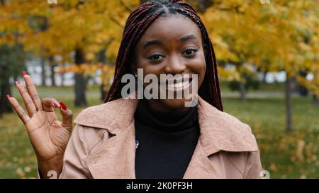 Primo piano giovane felice ragazza afroamericana felice guardando la macchina fotografica in posa all'aperto mostrando ok gesto di approvazione raccomandazione segno buona scelta Foto Stock