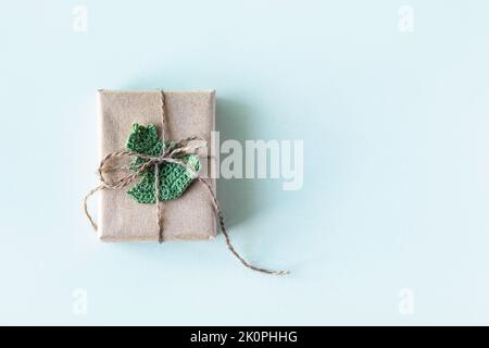 Scatola regalo in carta artigianale grigia decorata con un albero di Natale a maglia verde su sfondo turchese per le vacanze, piatto Foto Stock