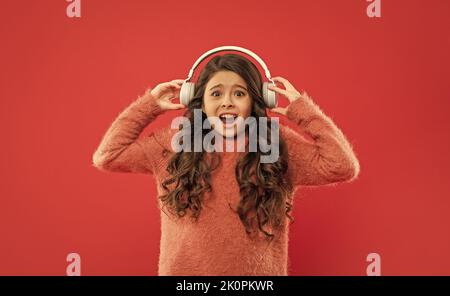 il bambino scioccato nel maglione ascolta musica ad alto volume in auricolari, musica Foto Stock