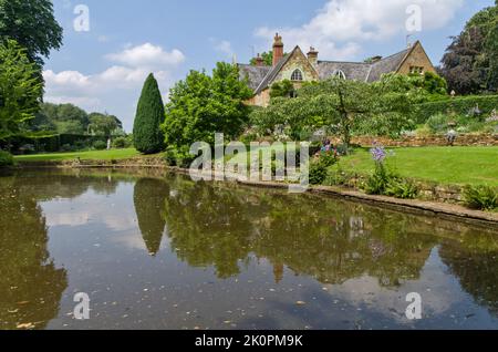 Una vista estiva sul lago ornamentale fino alla casa padronale, Coton Manor Gardens, vicino a Guilsborough, Northamptonshire, Regno Unito Foto Stock