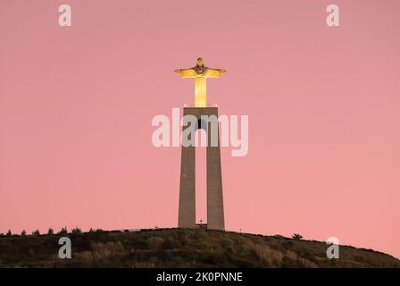 Cristo Re, statua di Cristo Rei ad Almada, Lisbona, Portogallo. Il monumento illuminato di Gesù Cristo visto dal fiume Tago durante il tramonto. Foto Stock