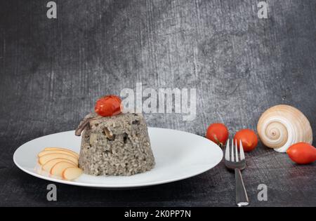 Piatto di riso che imita pesce e inchiostro nero di calamari, servito su un piatto con mela e pomodoro. Sullo sfondo pomodori e un cozze. Il backgro grigio Foto Stock