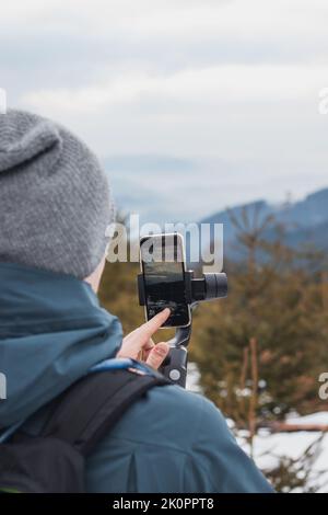 giovani yutuber vlogs sui suoi social network utilizzando un telefono cellulare e un gimbal per video migliori. Registrazione invernale. Atleta. Dettagli sulla trasmissione video Foto Stock