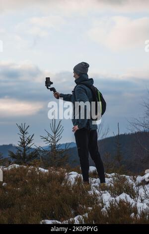 giovani yutuber vlogs sui suoi social network utilizzando un telefono cellulare e un gimbal per video migliori. Registrazione invernale. Atleta. Foto Stock