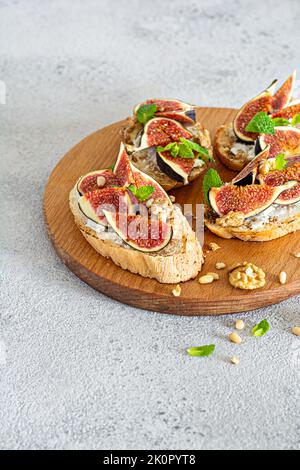 Bruschetta croccante con ricotta morbida, fichi maturi, noci e pinoli, menta e miele su un asse di legno su fondo chiaro. Foto Stock