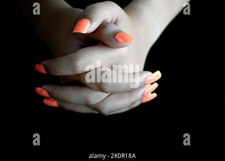 Fuoco selettivo delle mani femminili intrecciate con unghie false arancioni, su sfondo nero. Manicure unghie Foto Stock