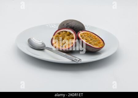 Due frutti di Passione su un piatto bianco su fondo bianco con un cucchiaio. Foto Stock
