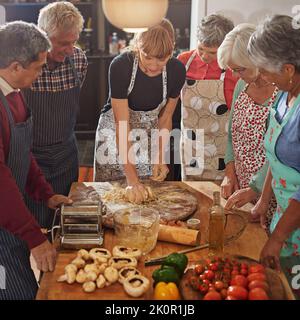 Niente riunisce le persone come il buon cibo. Un gruppo di anziani che frequentano una lezione di cucina. Foto Stock