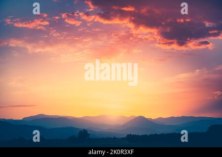 Spettacolare alba sulla catena montuosa sotto la nebbia alla luce del mattino. Nuvole colorate nel cielo arancione. Paesaggio naturale sorprendente sfondo. Turismo e viaggio immagine concettuale. Spazio di copia. Foto Stock