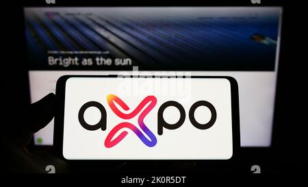 Persona che tiene un telefono cellulare con il logo della società svizzera dell'energia Axpo Holding AG sullo schermo davanti alla pagina web aziendale. Messa a fuoco sul display del telefono. Foto Stock
