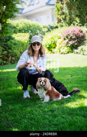 Ritratto di felice donna di mezza età con i suoi cuccioli carini che si rilassano nel cortile a casa. Foto Stock