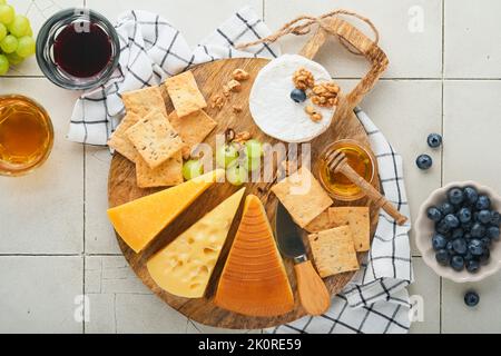 Assortimento di formaggi, miele, cracker, mirtilli, uva con vino rosso e bianco in bicchieri antipasto server su tavola di marmo bianco su fondo grigio Foto Stock