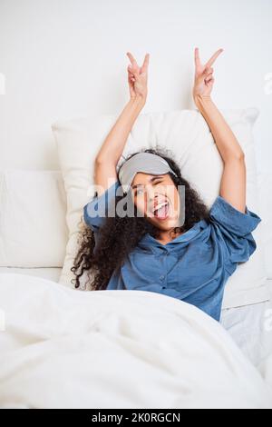 Una bella giovane donna multietnica mostra segni di pace svegliarsi a letto Foto Stock