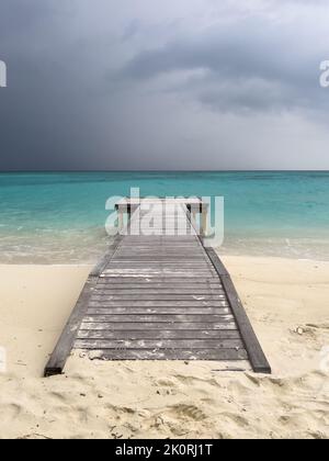 Un molo vuoto in legno che conduce dalla spiaggia alle acque turchesi dell'oceano su un'isola delle Maldive. Foto Stock