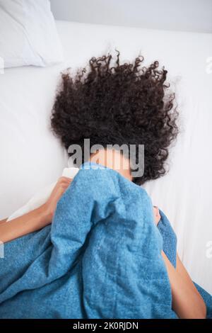 Foto aerea di una giovane donna dai capelli ricci che si nasconde sotto una coperta blu Foto Stock
