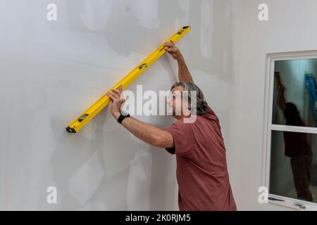 Prima di dipingere un muro di cartongesso, un dipendente si assicura che sia a livello utilizzando un livello Foto Stock