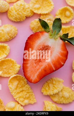 metà di fragola fresca tagliata intorno a croccanti fiocchi di mais su rosa, immagine stock Foto Stock