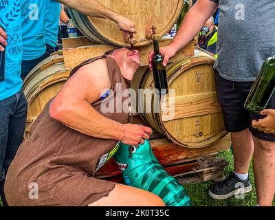 Un corridore vestito da Fred Flintstone beve direttamente dal rubinetto di una botte di vino allo Château Larose-Trintaudon a Saint-Laurent-Médoc, in Francia, durante il 36° Marathon des Châteaux du Médoc, evitando il bicchiere che gli viene offerto. Il maratona è noto per servire vino rosso lungo il suo percorso. Con una torre costruita nel 1884 e una delle più grandi aree viticole del Médoc, lo Château Larose-Trintaudon è tra le stazioni notevoli del maratona lungo le sue 25 cantine. Foto Stock
