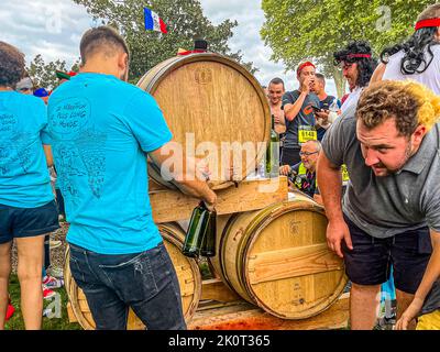 A Château Larose-Trintaudon a Saint-Laurent-Médoc, in Francia, un aiutante versa vino rosso direttamente da una botte barrique nei bicchieri durante il 36° Marathon des Châteaux du Médoc – il vintage 2015 scorre direttamente dal rubinetto. Un corridore indossa una maglietta con la scritta "Le Marathon le plus long du monde" ("Il maratona più lungo del mondo"), con una bandiera francese che sventola sopra la scena. Foto Stock