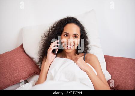 Primo piano di una giovane donna multietnica che chiacchiera sul cellulare in letto con cuscini Foto Stock