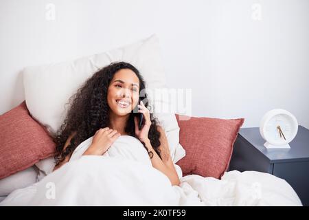 Una giovane donna multietnica ride durante la chiamata intima a lunga distanza dal letto Foto Stock