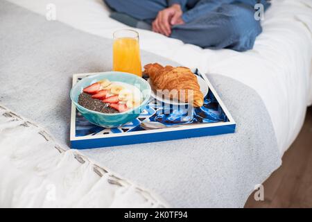 Primo piano del vassoio della colazione con croissant, frutta ciotola a letto con donna seduta Foto Stock