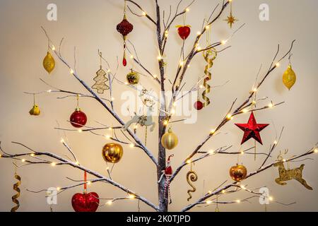Decorazioni dell'albero di Natale in rosso tradizionale e oro appesi su un moderno albero di Twig con effetto neve Foto Stock