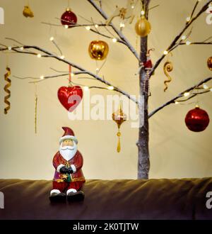La figura di Natale del Babbo Natale sedette davanti ad un albero di Natale del Twig dell'albero decorato nel rosso e nell'oro tradizionali Foto Stock