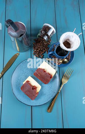 Guava dolce con formaggio circondato da posate, tazza e chicchi di caffè su un tavolo blu verticale e vista dall'alto. Foto Stock