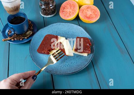 Donna che tiene con una forchetta pezzi di guava dolce con formaggio, circondato da fagioli e tazza di caffè. Foto Stock