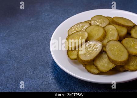 Deliziosi cetrioli salati in scatola tagliati a fette su un piatto di ceramica bianca su uno sfondo di cemento scuro Foto Stock