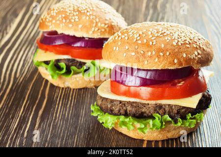 Due cheeseburgers fatti in casa con polpettine di manzo e insalata fresca su conigli di condimenti, serviti su un tavolo di legno marrone. Foto Stock